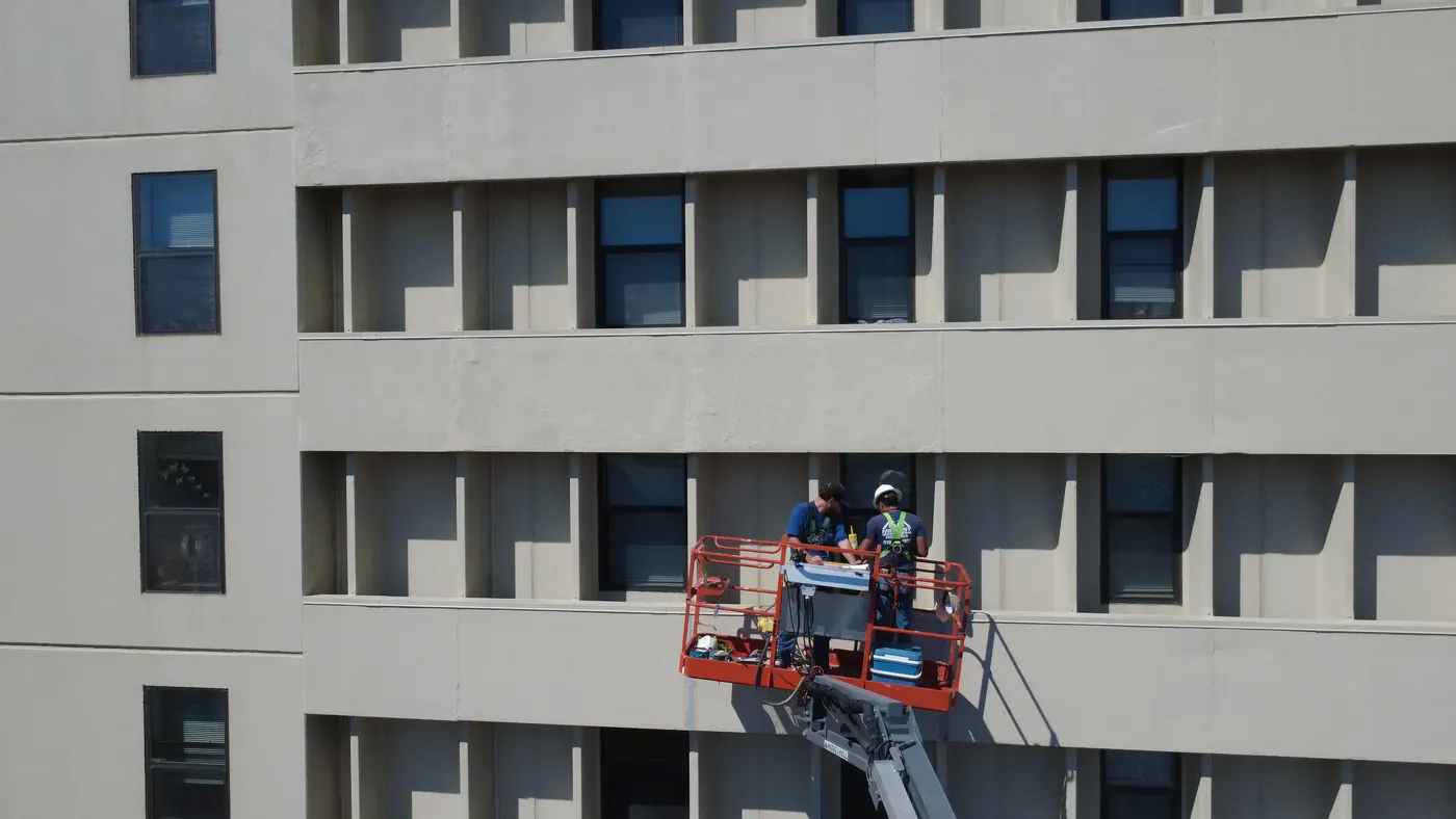Two Midwest crew members in hard hats and harnesses working from a boom lift basket