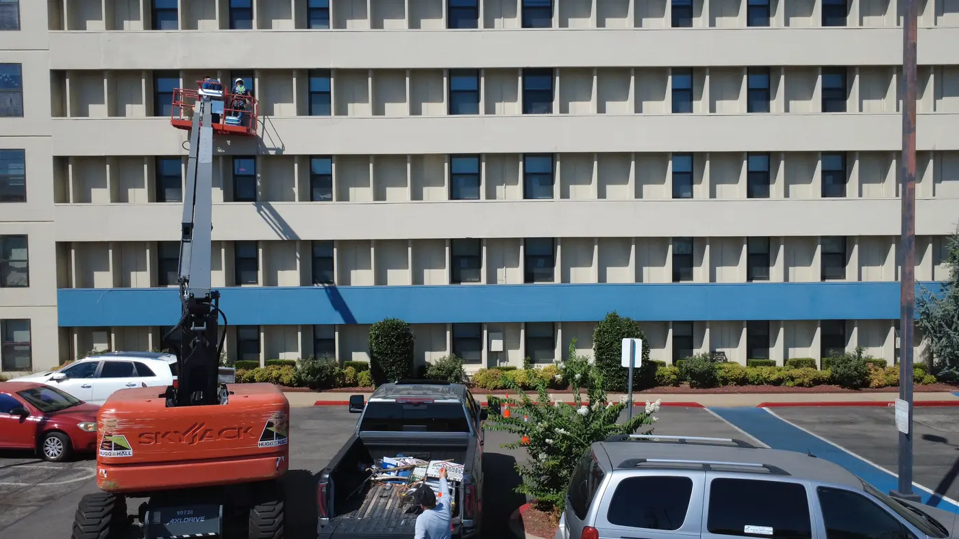 A boom lift extended against a seven-storey commercial building with crews working the facade